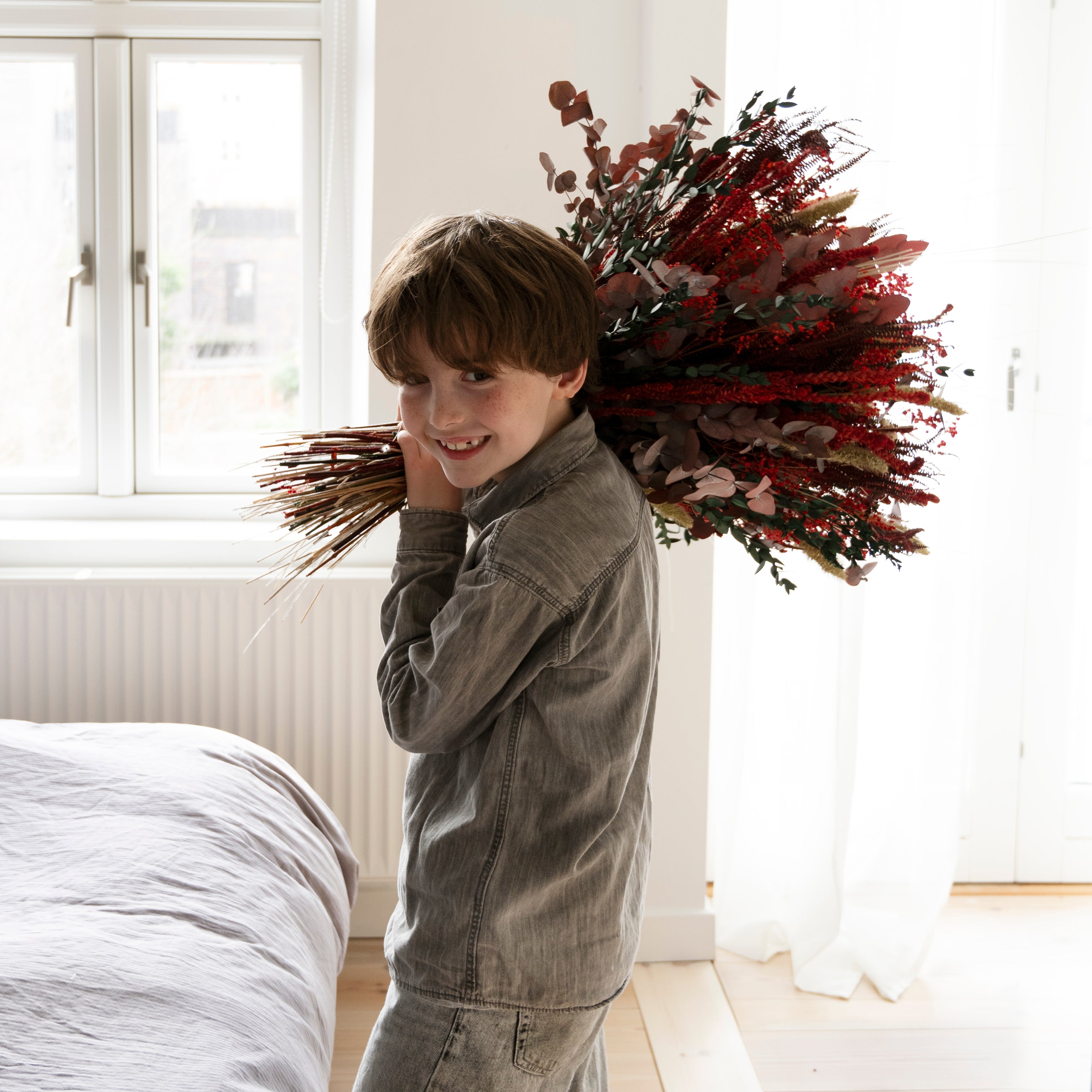 Lächelnder Junge trägt einen großen roten Living Flowers Blumenstrauß auf der Schulter