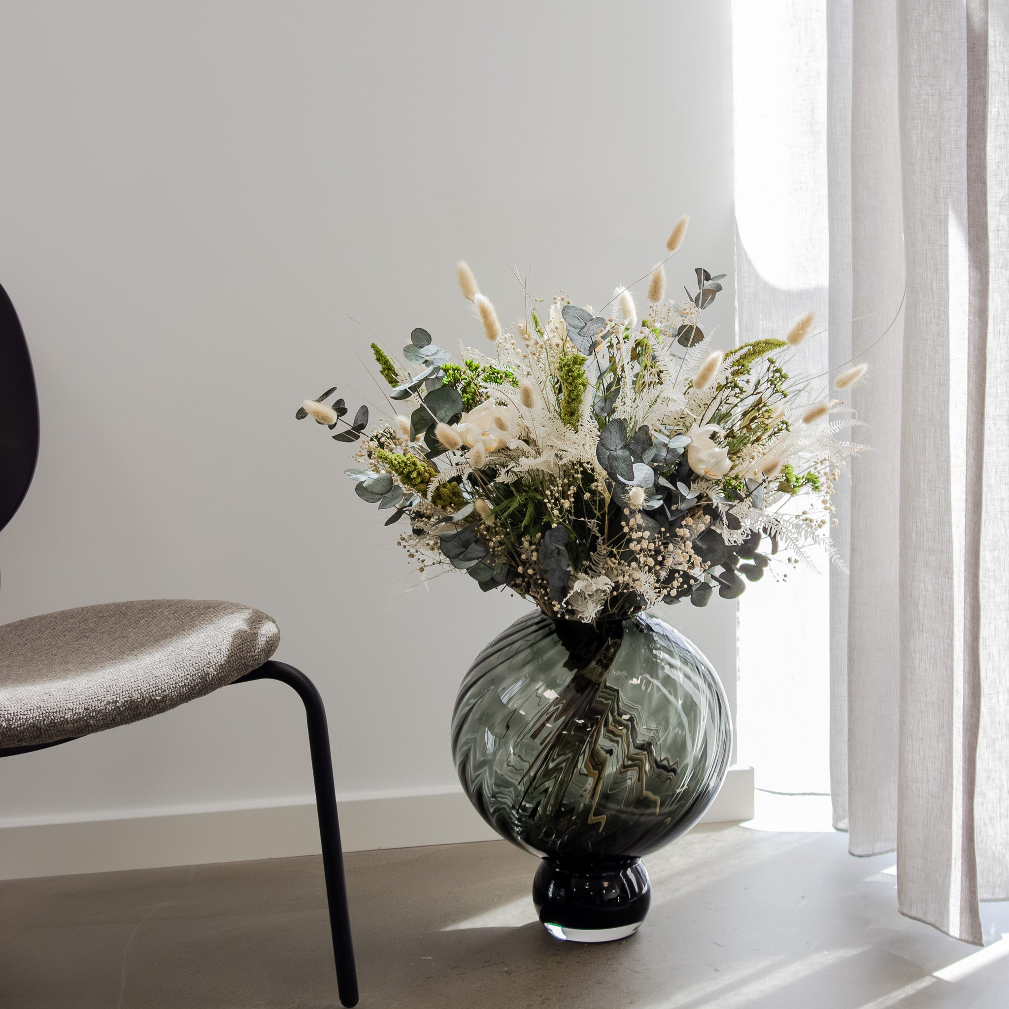 In einem Zimmer steht eine große bauchige Vase, in der ein voller grün-weißer Blumenstrauß steht