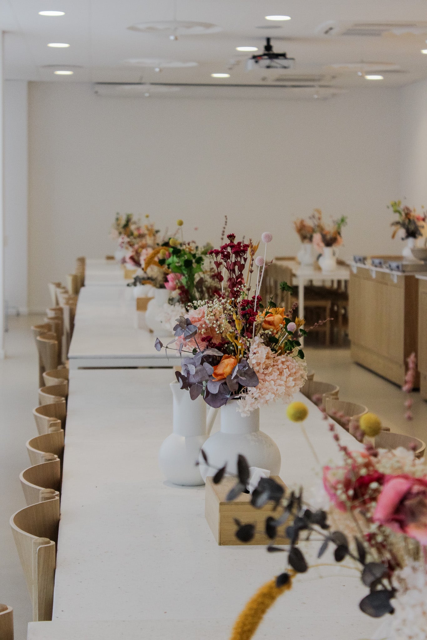 Auf einer langen Tafel in einem Pausenraum stehen viele kleine Vasen, in denen langlebige Blumen stecken