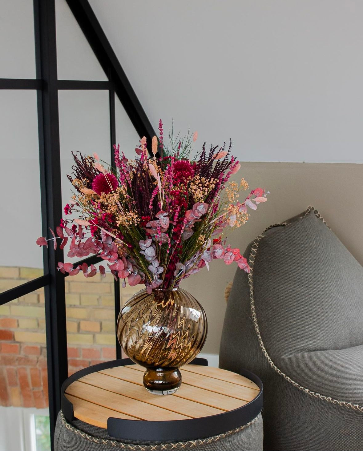 Ein Blumenstrauß in kräftigen Rot- und Pinktönen stehet in einer Vase auf einem Beistelltisch