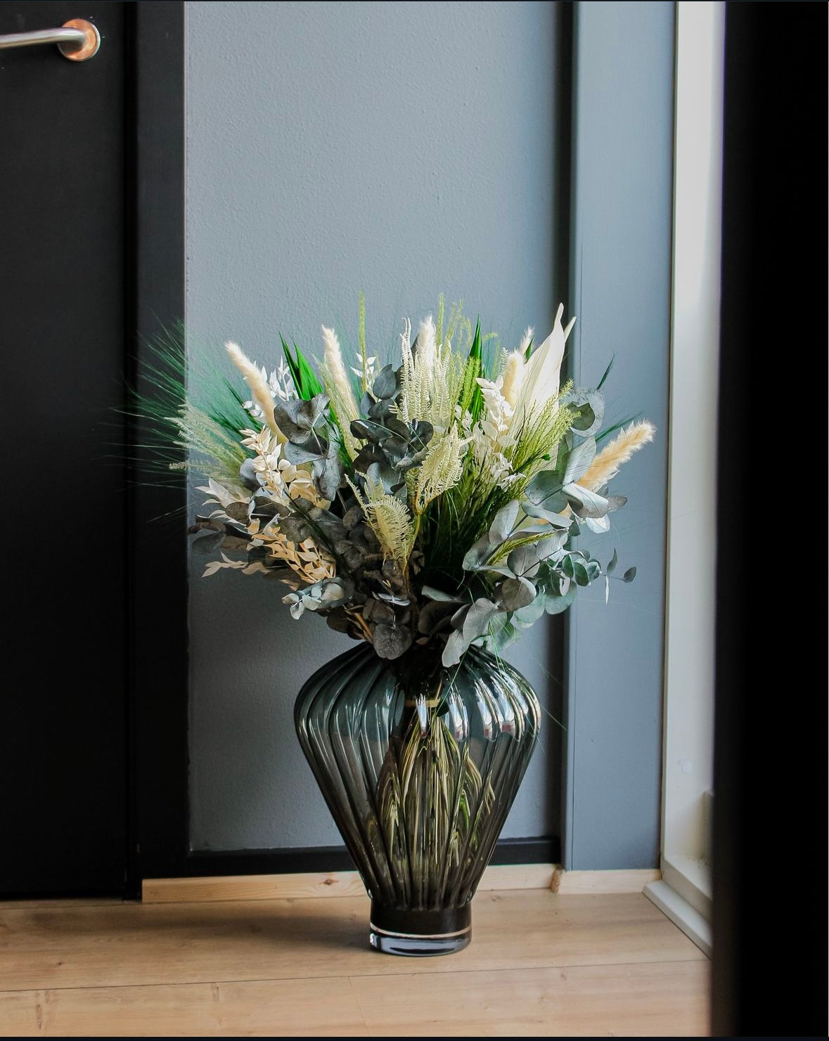 In einem Wohnraum steht eine große geometrische Vase auf dem Boden, in ihr steht ein grün-weißer Blumenstrauß