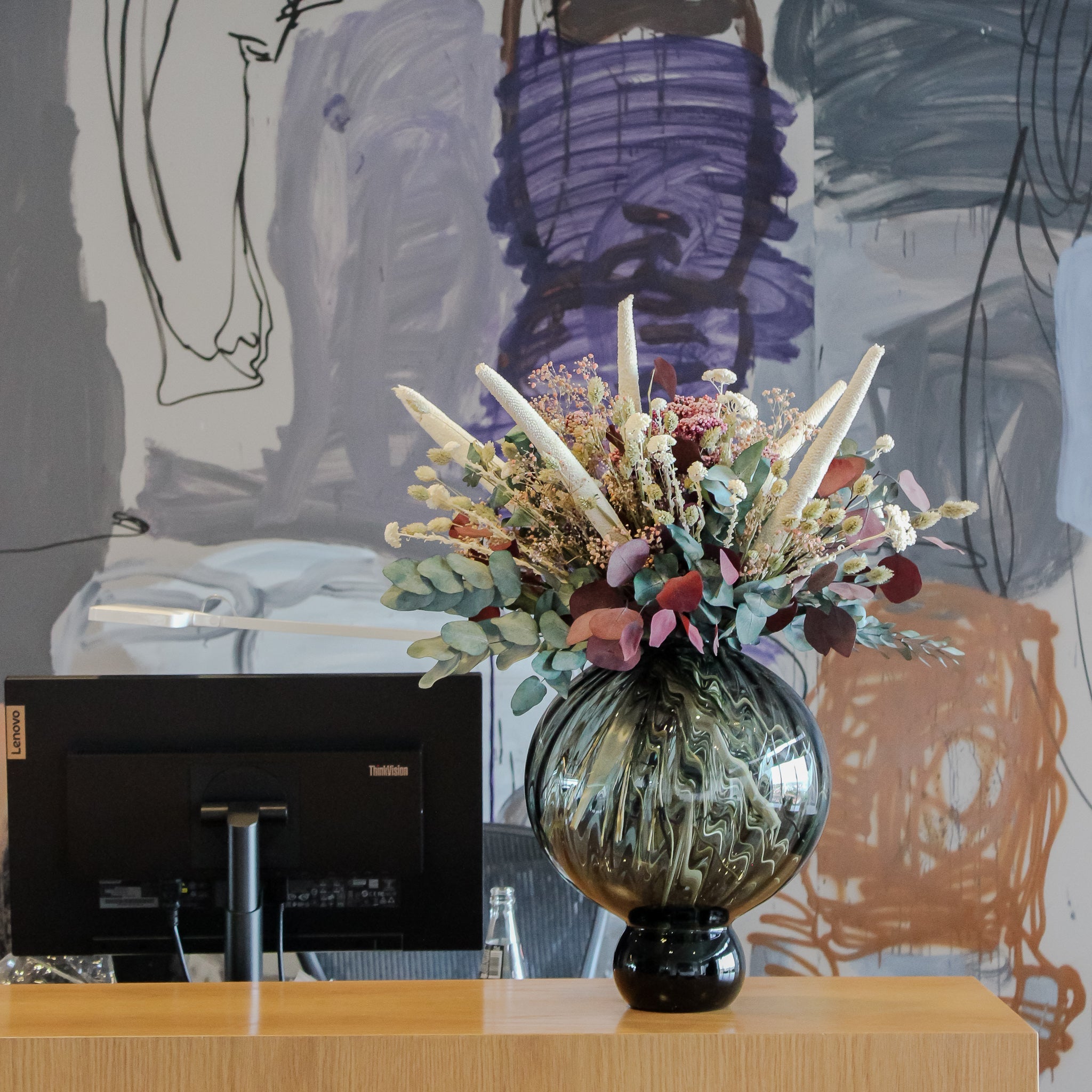 Auf einem Schreibtisch steht eine bauchige Vase mit auffälligen Blumen