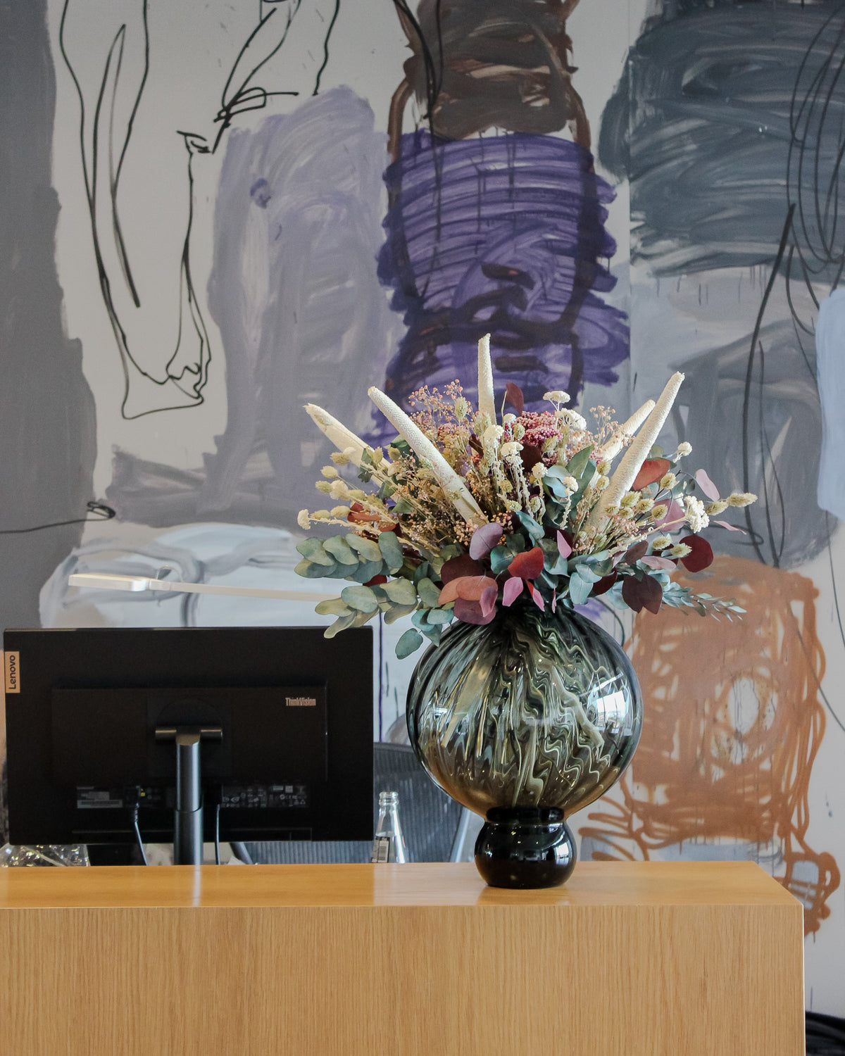 På et skrivebord står en rund vase med iøjnefaldende blomster.