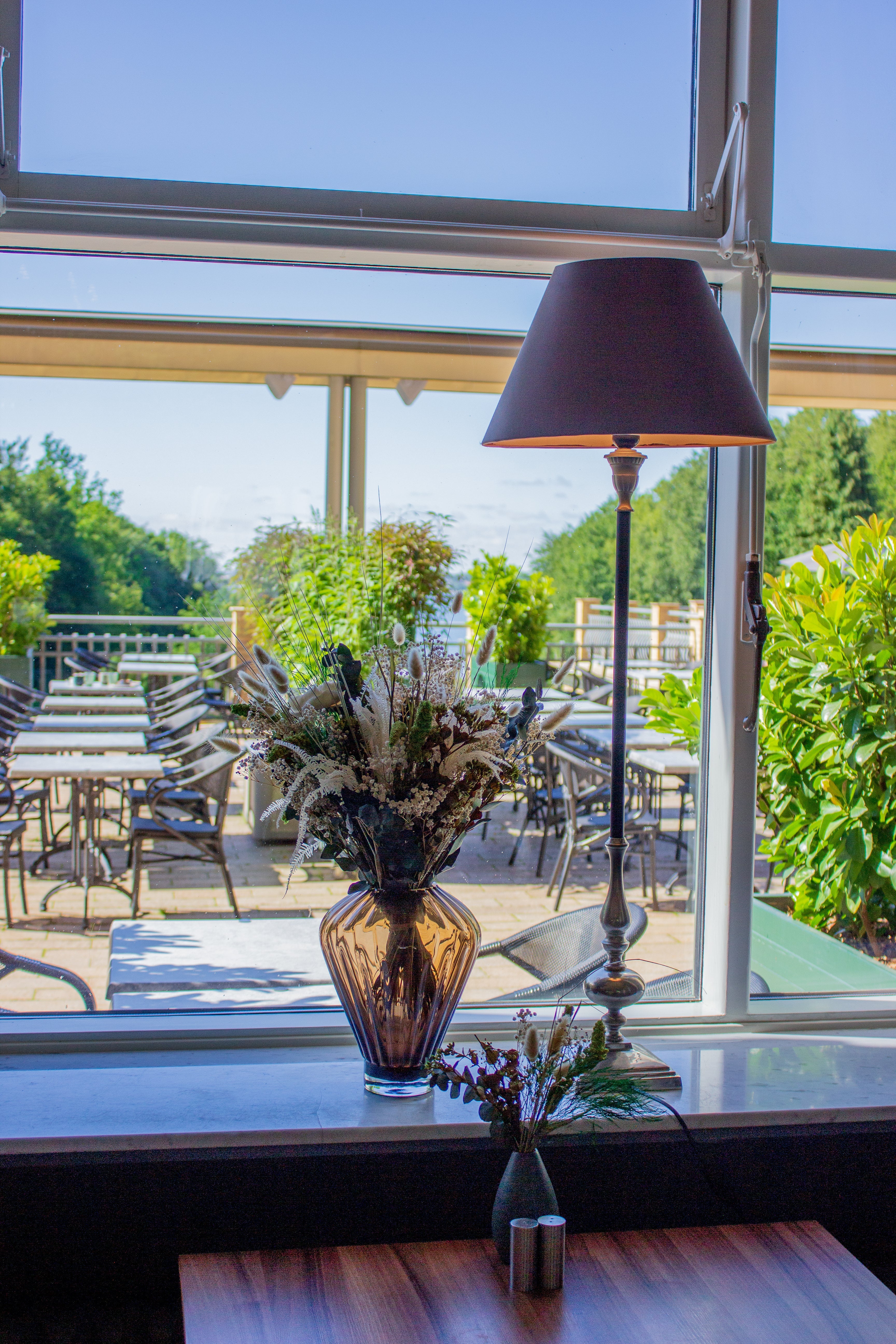 Auf der Fensterbank eines Restaurants steht eine geometrische Glasvase mit einem grün-weißen Blumenstrauß 