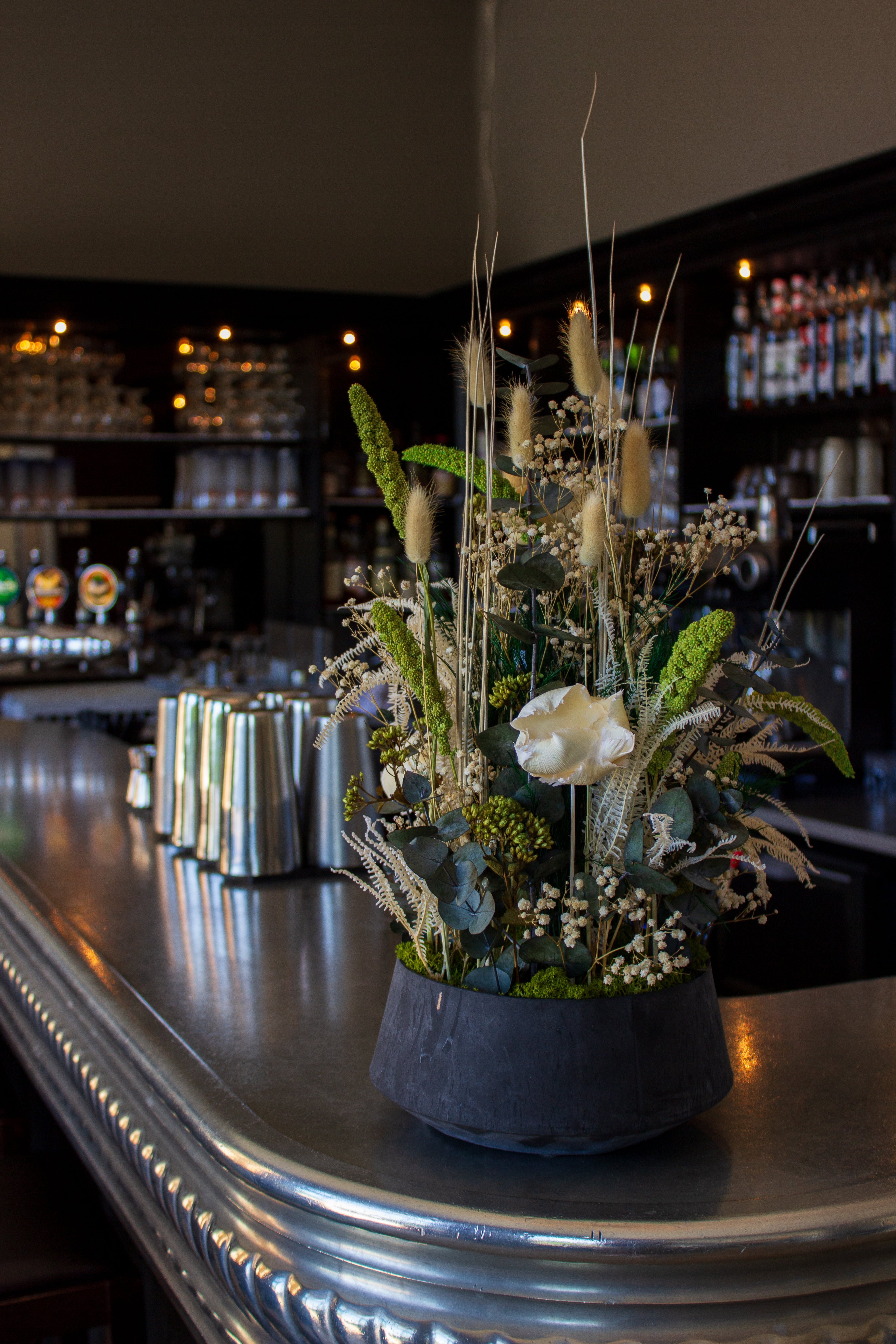 Auf einem Bartresen steht eine eindrucksvolle Blumendekoration in natürlichen weiß-grünen Nuancen in einer Schale