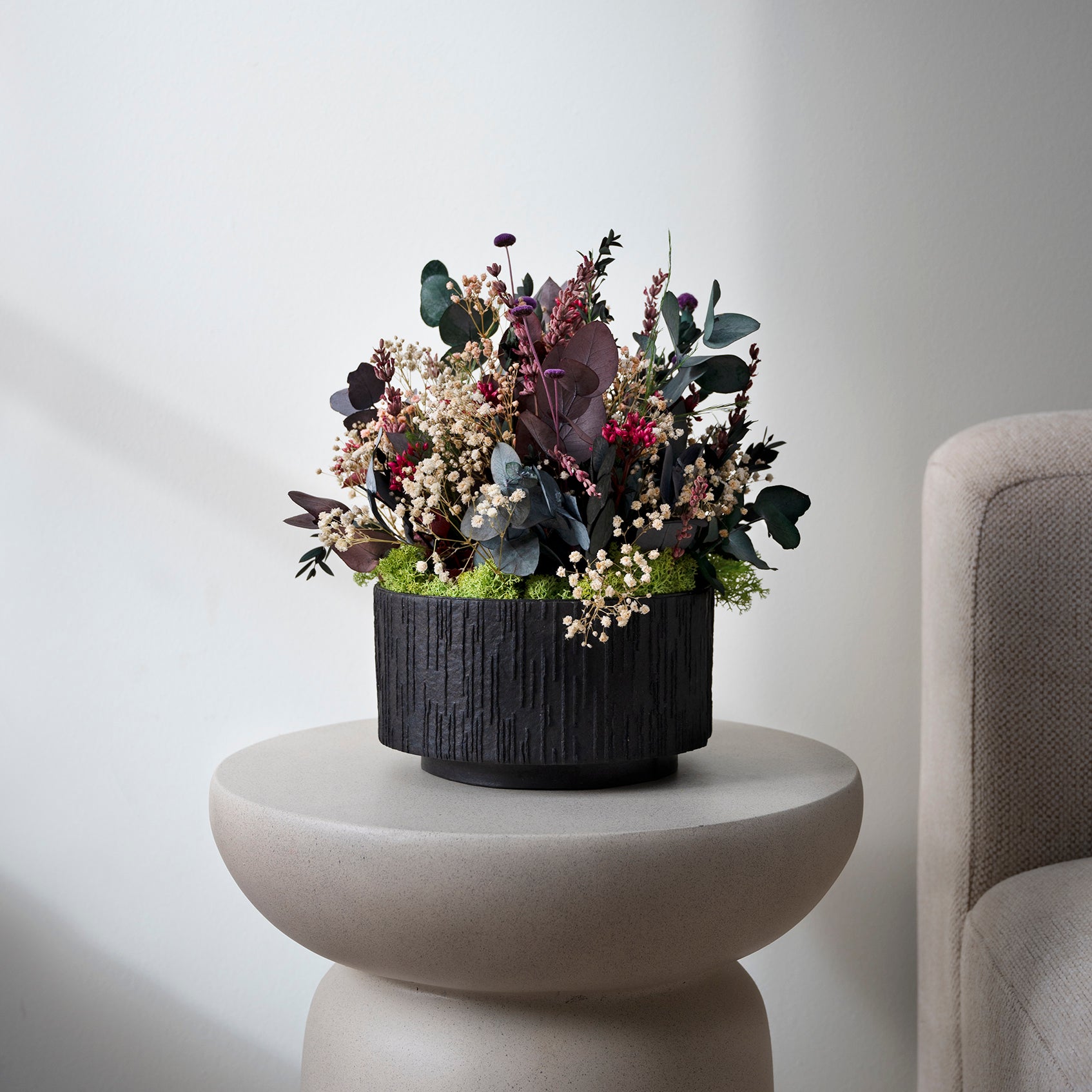 Langlebige Living Flowers Blumendekoration in schwarzem Topf auf einem modernen Beistelltisch.