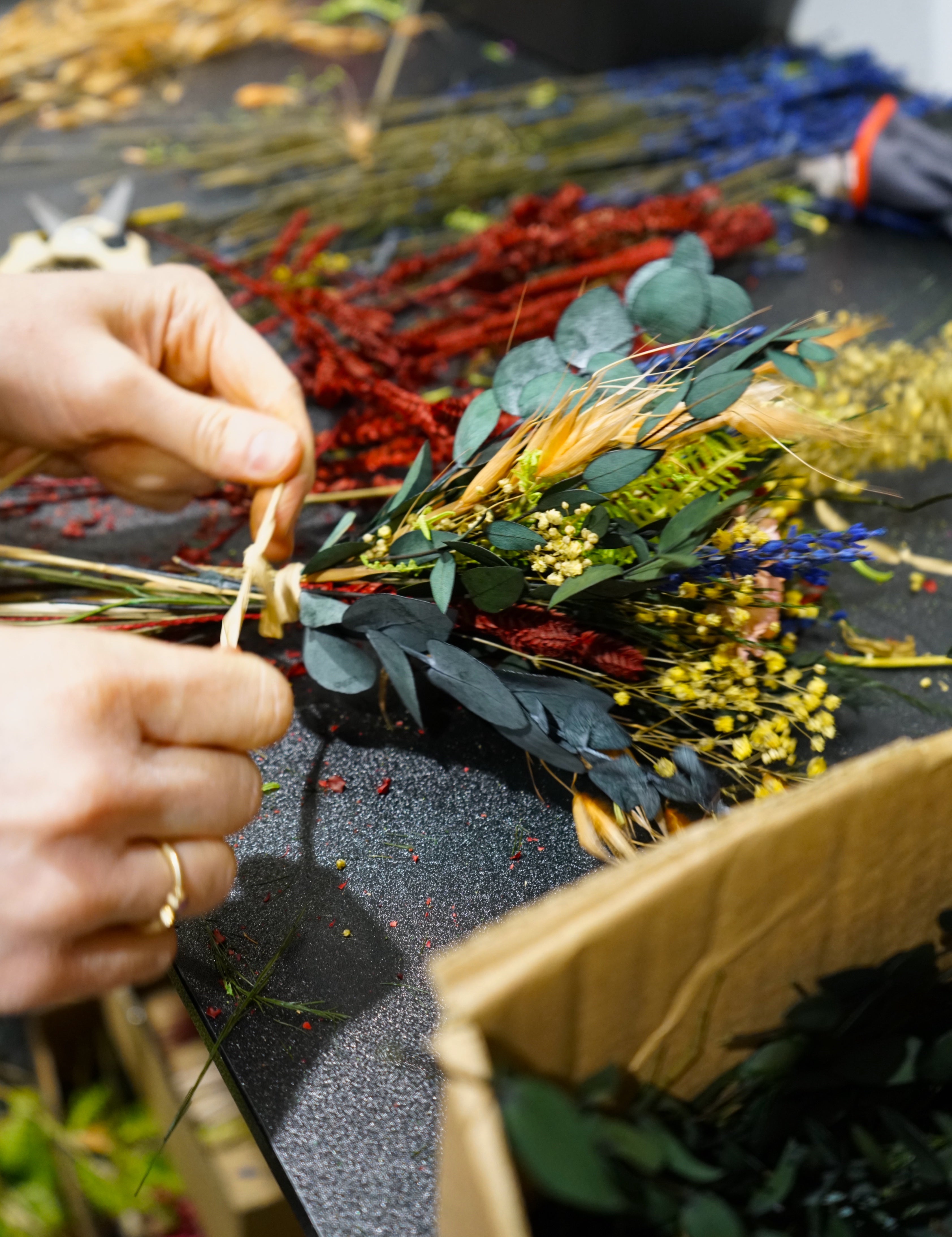 „Floristin bindet einen Living Flowers Blumenstrauß aus bunten langlebigen Blumen wie Eukalyptus, rotem Amaranth und gelben Blüten
